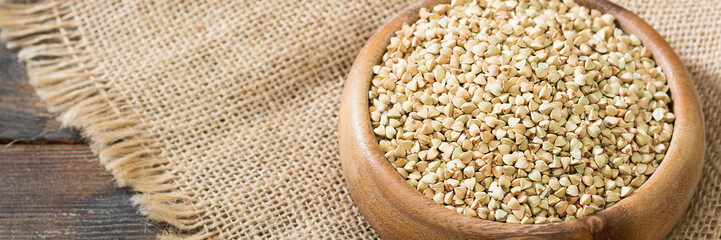 Green buckwheat in a wooden bowl on a brown wooden table. Superfood in a bowl. Green buckwheat close-up. The view from the top. Banner with space for text