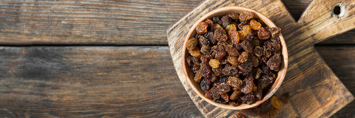 Raisins in a wooden bowl on the brown kitchen table. Raisins close-up. The view from the top. Banner with space for text
