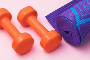 Dumbbell and gymnastic mat on a pink background close-up