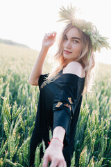 Young, slender girl in a wreath of wheat ears at sunset in a field