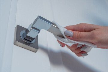 Woman cleaning door handle with antiseptic disinfectant wet wipe - low angle close up. Disinfection, protection, prevention, housework, COVID 19, coronavirus, safety, sanitation concept