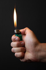 Lighter in hand. A flame bursts out of the lighter. Black background, vertical photo