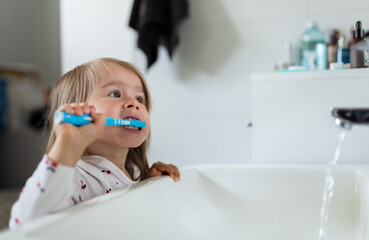 Baby girl in bright bathroom brushing her teeth above the sink.