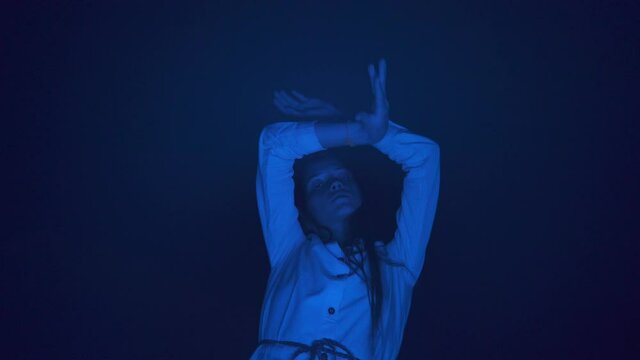 Slow ecstatic dance of young beautiful long haired woman in white dress in the darkness. Blue light. Low angle shot. Night club dancing party. Freedom mood.
