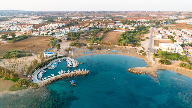 Aerial bird's eye view of coastline sunset, landmark white washed chapel Agia Triada beach, Protaras, Famagusta, Cyprus from above. Tourist attraction Ayia Trias bay church, sand, port at sunrise.