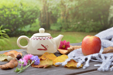 teapot on a wooden table in garden among autumnal  leaf and red apple on wool scarf