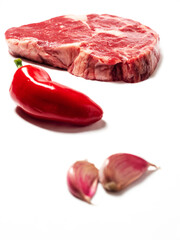 Rib eye steak in focus, red hot chilli pepper and two garlic cloves out of focus, premium cut of beef, Meat industry. White background.