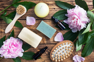 Fototapeta na wymiar Concept SPA and Wellness. Massage brush, cosmetic oils and soap. Wooden background with peony flowers.
