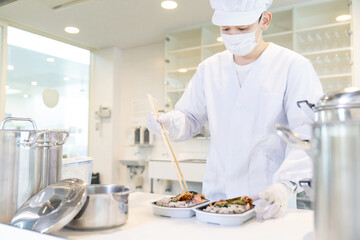 弁当を盛り付ける男性調理師　宅食　デリバリー　テイクアウト