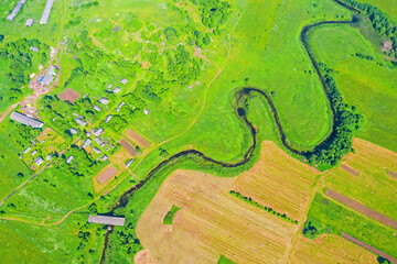 Top aerial view of the natural rural landscape valley of a meandering river among green fields and forests.