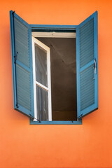 Open window with wooden blue shutters in a house with orange walls. Close-up. Vertical.