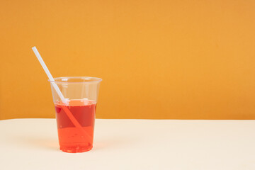 Red sparkling water in plastic cup with straw on table.