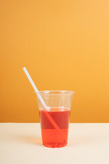 Red sparkling water in plastic cup with straw on table.