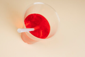 Red sparkling water in plastic cup with straw on table. Close up.