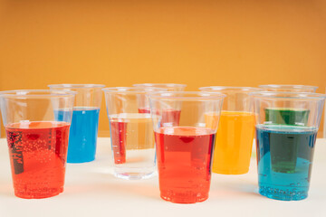 Glasses of various colors and tastes soda drink on orange background. Red, blue, soda, orange, green sparkling water on table with copy space.