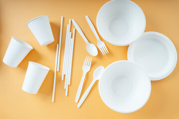 Disposable plastic cup, fork, spoon, bowl, pan,and straw over orange background.