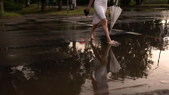 a girl in a white dress walks through puddles after the rain