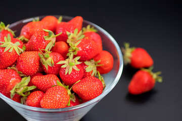 Fresh organic strawberries in  glass bowl  on  black table.