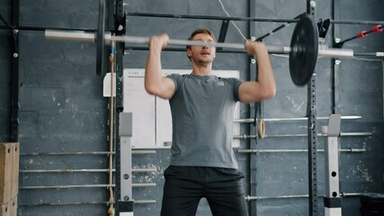 Slow motion of handsome young sportsman lifting barbell training in gym alone focused on power exercise. Modern youth, lifestyle and bodycare concept.