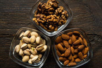 Almond, pistachio and walnut in a small plates which standing on a vintage wooden table. Nuts is a healthy vegetarian protein and nutritious food.