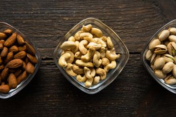 Almond, pistachio and cashew in a small plates which standing on a vintage wooden table. Nuts is a healthy vegetarian protein and nutritious food.