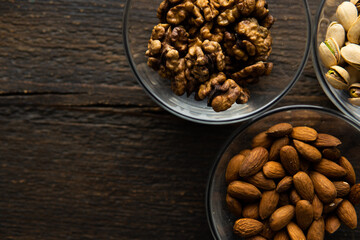 Almond, pistachio and walnut in a small plates which standing on a vintage wooden table. Nuts is a healthy vegetarian protein and nutritious food.