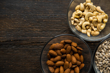 Almond, cashew and sunflower seeds in a small plates which standing on a vintage wooden table. Nuts is a healthy vegetarian protein and nutritious food.