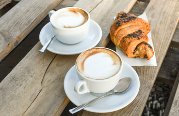 Two cups of cappuccino with latte and croissant on wooden background. stylish toning. morning coffee for couple in love.