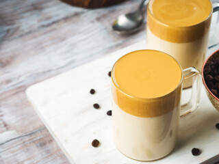 Whipped dalgona coffee drink in transparent mug on white wooden board. Cozy breakfast