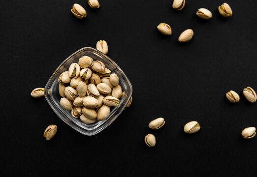 Pistachios in a small plate with scattered nuts of almonds around a plate on a black surface. Pistachio is a healthy vegetarian protein nutritious food. Natural nuts snacks.