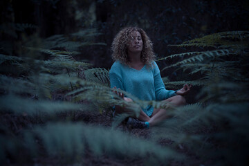 Relaxed woman in minduflness exercises or yoga meditation sit down in the middle of a green forest...