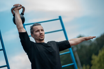 young athlete has workout and doing sport exercises with kettlebell outdoor
