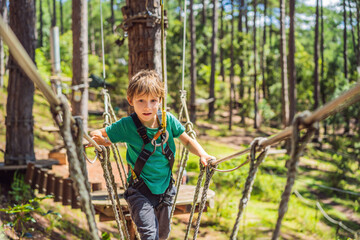 Naklejka na ściany i meble Portrait of cute little boy walk on a rope bridge in an adventure rope park