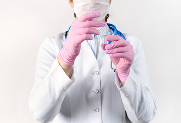 Cropped view of young female doctor in a white coat, in a medical mask and pink sterile gloves holding ampoule vaccines for children or older adults. Concept: diseases, medical care, diabetes.