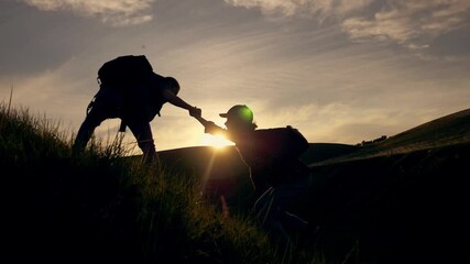 Teamwork. Travelers lend a helping hand, overcoming obstacles, climbing to the top. Business, the path to success. Silhouette of tourists at sunset in the mountains in the sun.