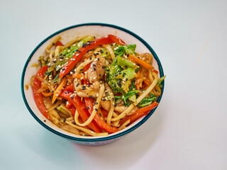 Udon noodles with meat in a plate on a white surface. With vegetables greens