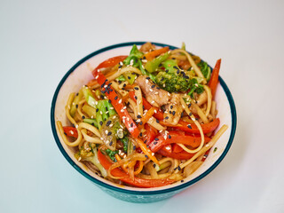 Udon noodles with meat in a plate on a white surface. With vegetables greens