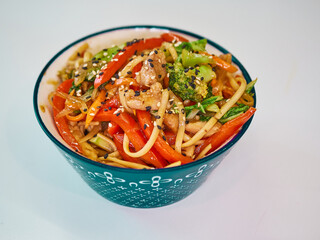 Udon noodles with meat in a plate on a white surface. With vegetables greens
