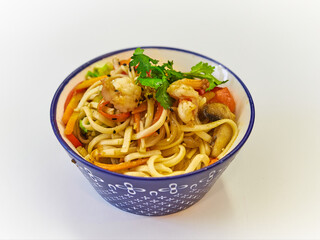 Udon noodles with seafood in a plate on a white surface. With vegetables greens