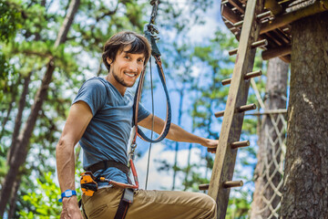 Young attractive man in adventure rope park in safety equipment