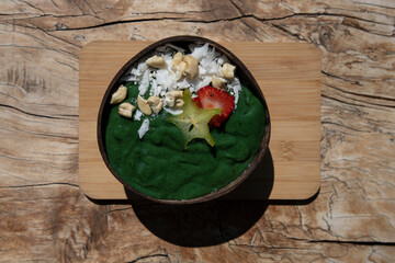 Fruit smoothie bowl with spirulina on wooden background, raw vegan diet