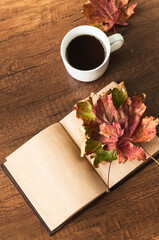 Clean book page, cup of coffee and autumn leaves on a wooden background.