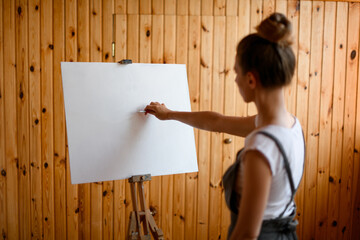 Young woman artist make sketch on canvas on wooden easel.