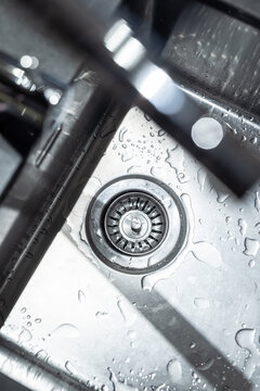 Modern water tap and sink, made of stainless steel. Drainage. Some water drops at the bottom.