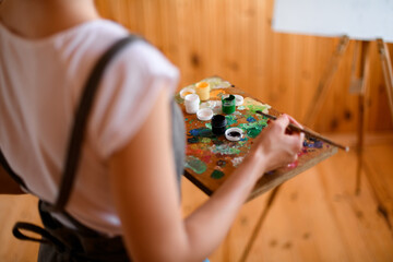 Close-up of palette with paints in the hands of woman artist.