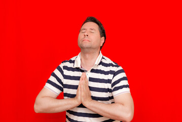 Calm middle age caucasian man wearing striped t shirt over isolated red trendy background praying...