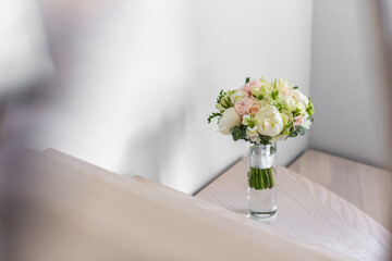 Wedding bouquet in a glass vase on the stairs near the wall.