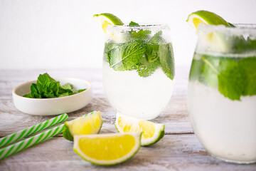 Summer refreshing drinks in glasses stand on a light wooden background. The glasses are decorated with a slice of lime; the edges of the glasses are coated with sugar. Near lie three slices of lime.