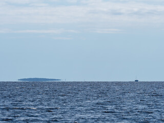 The island and the yacht on the horizon on the lake in hot weather look like a mirage
