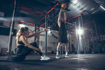 Beautiful young sporty couple workout in gym together. Caucasian man training with female trainer. Concept of sport, activity, healthy lifestyle, strength and power. Working out with weights.